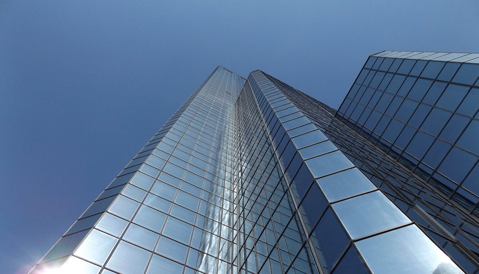 Low-angle view of a very tall glass/mirrored building against a pure blue sky