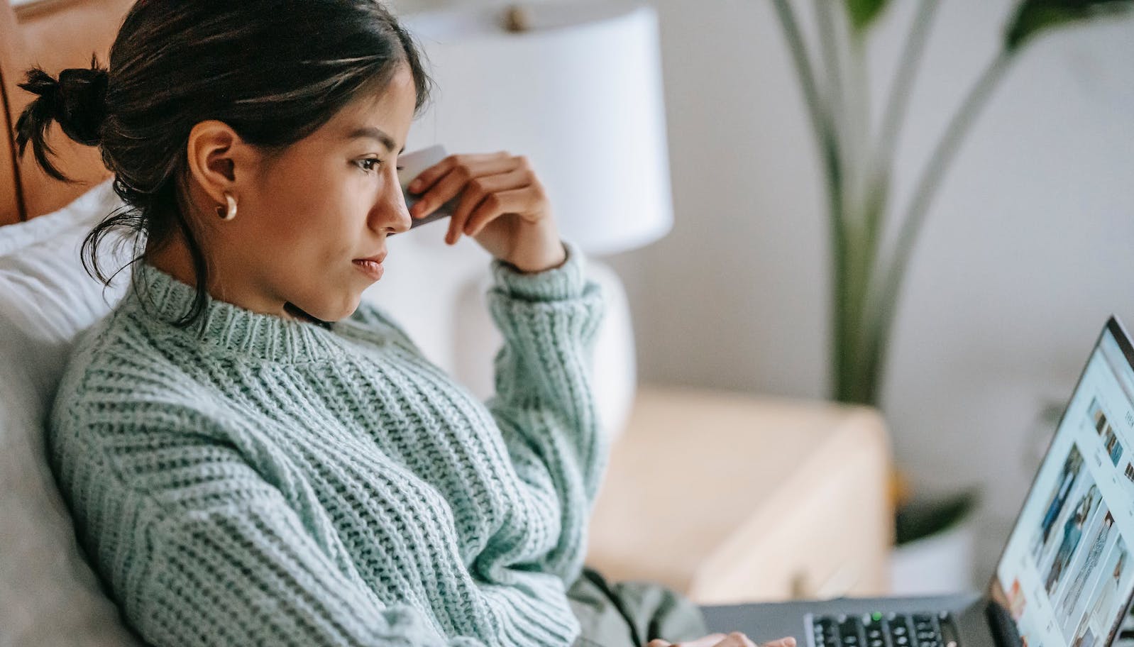 Woman sitting on a bed with a computer on her lap and looking contemplative