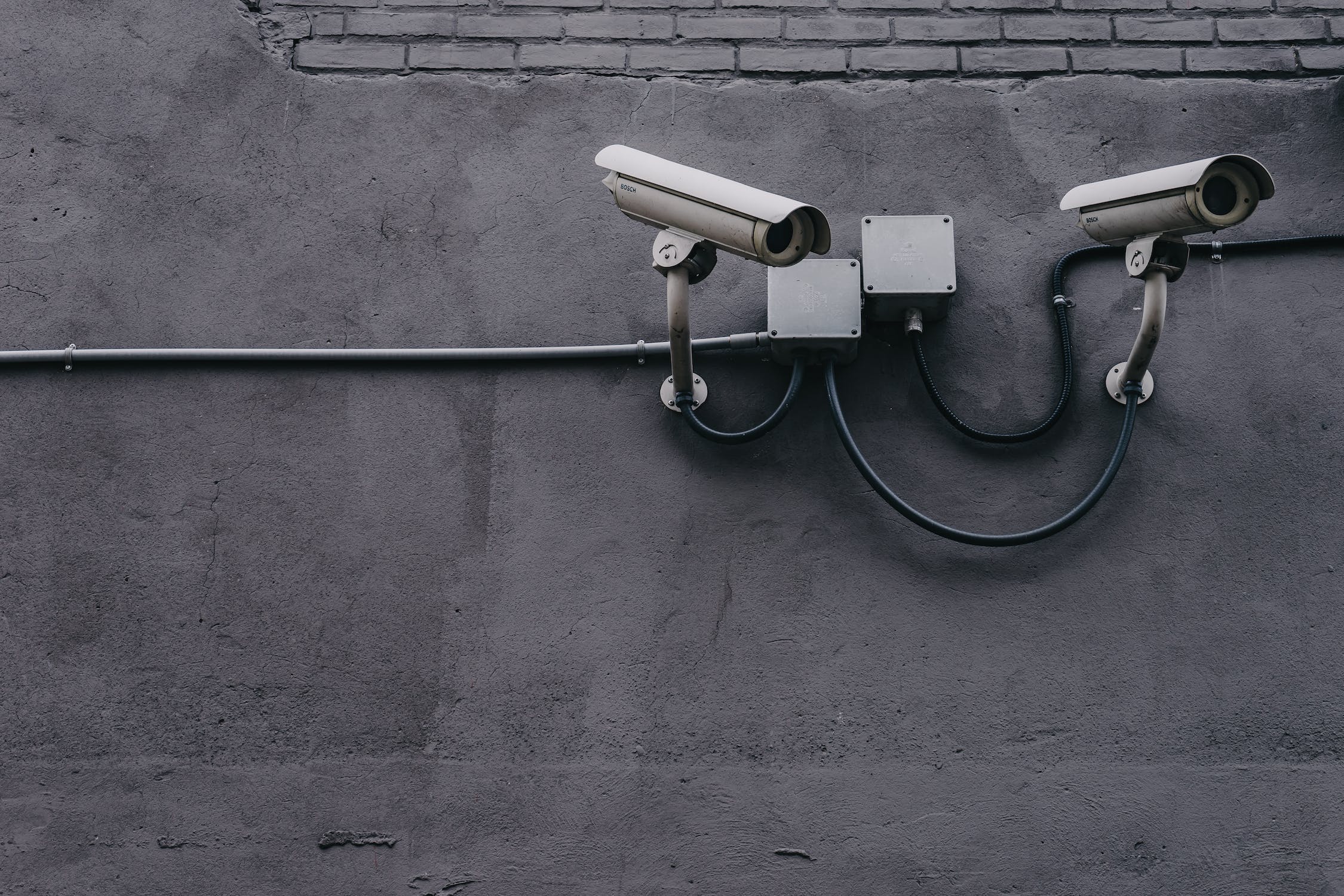 Two security cameras at the top right of a dark grey wall