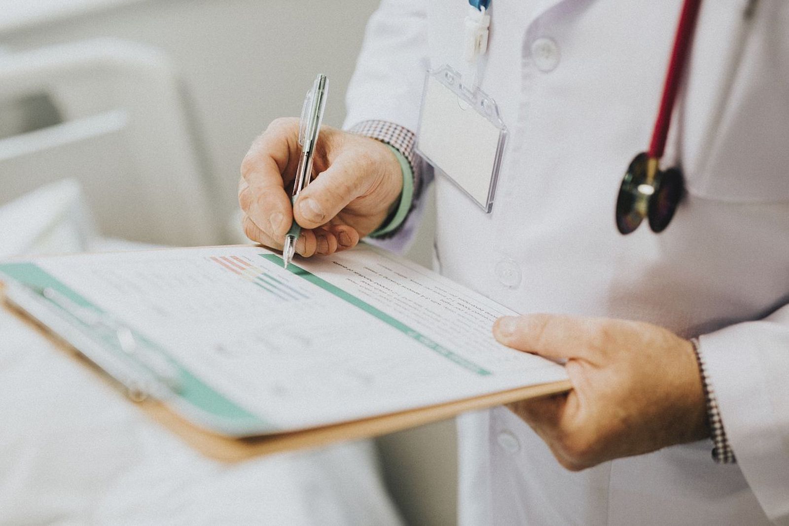 Doctor in a white coat holding a clipboard with a stethoscope and writing something