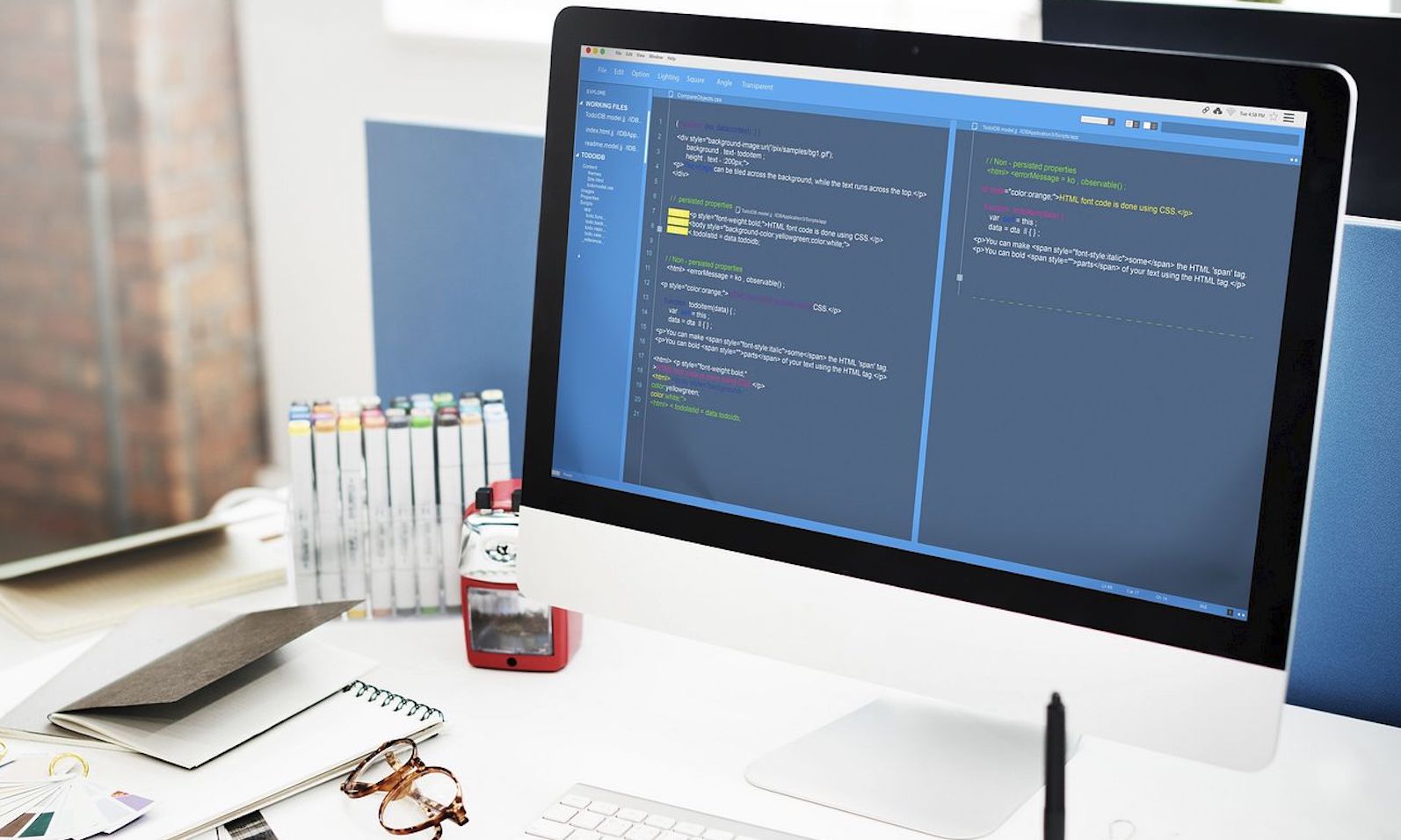 A desktop computer with code on it and on top of a white desk with a keyboard and pens