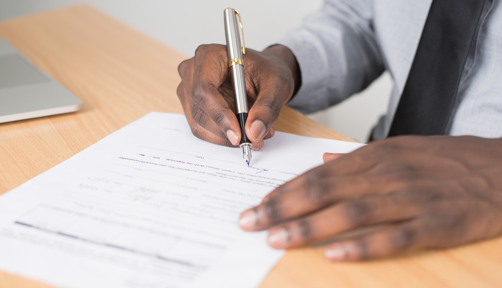 Close up image showing a person's hands as they sign a piece of paper on top of a wooden table