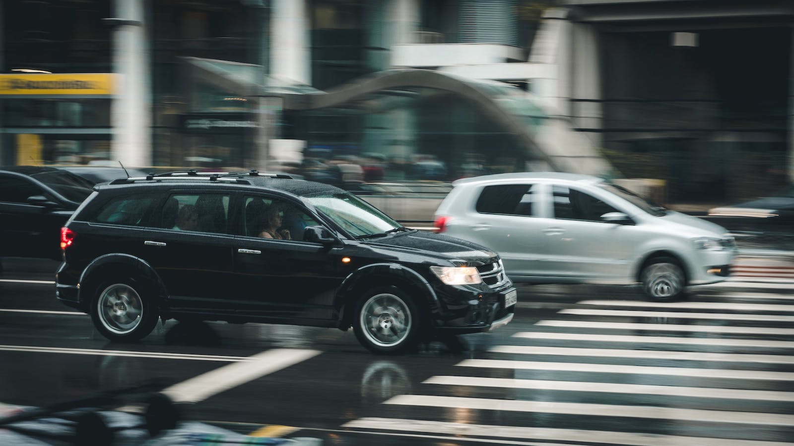 A black car and a silver car on the road with the background blurred