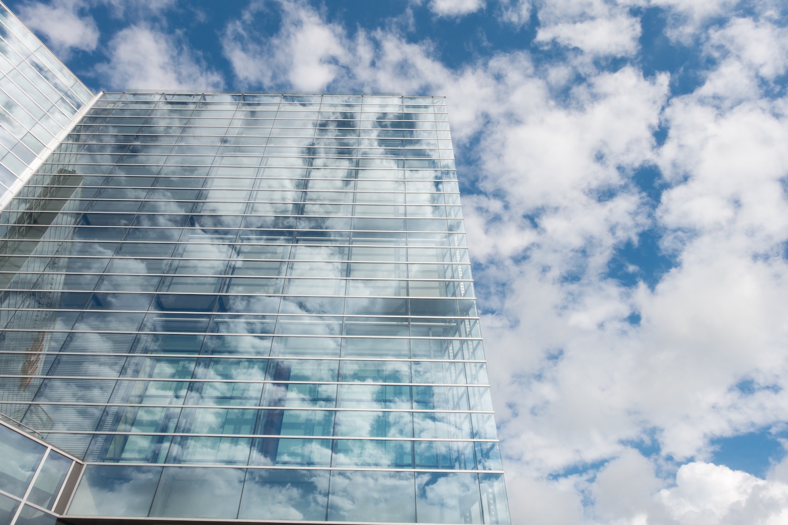 A tall glass building surrounded by clouds and in front of a blue sky that makes it look almost transparent