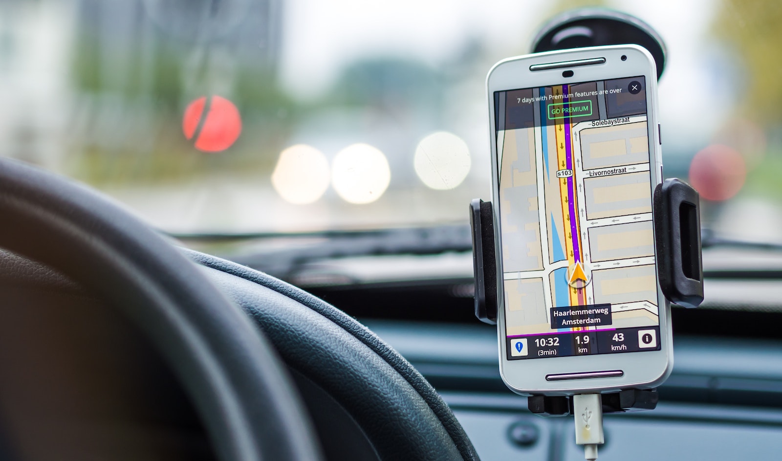 Close-up image of a smartphone with a map on the screen and on the dashboard of a car