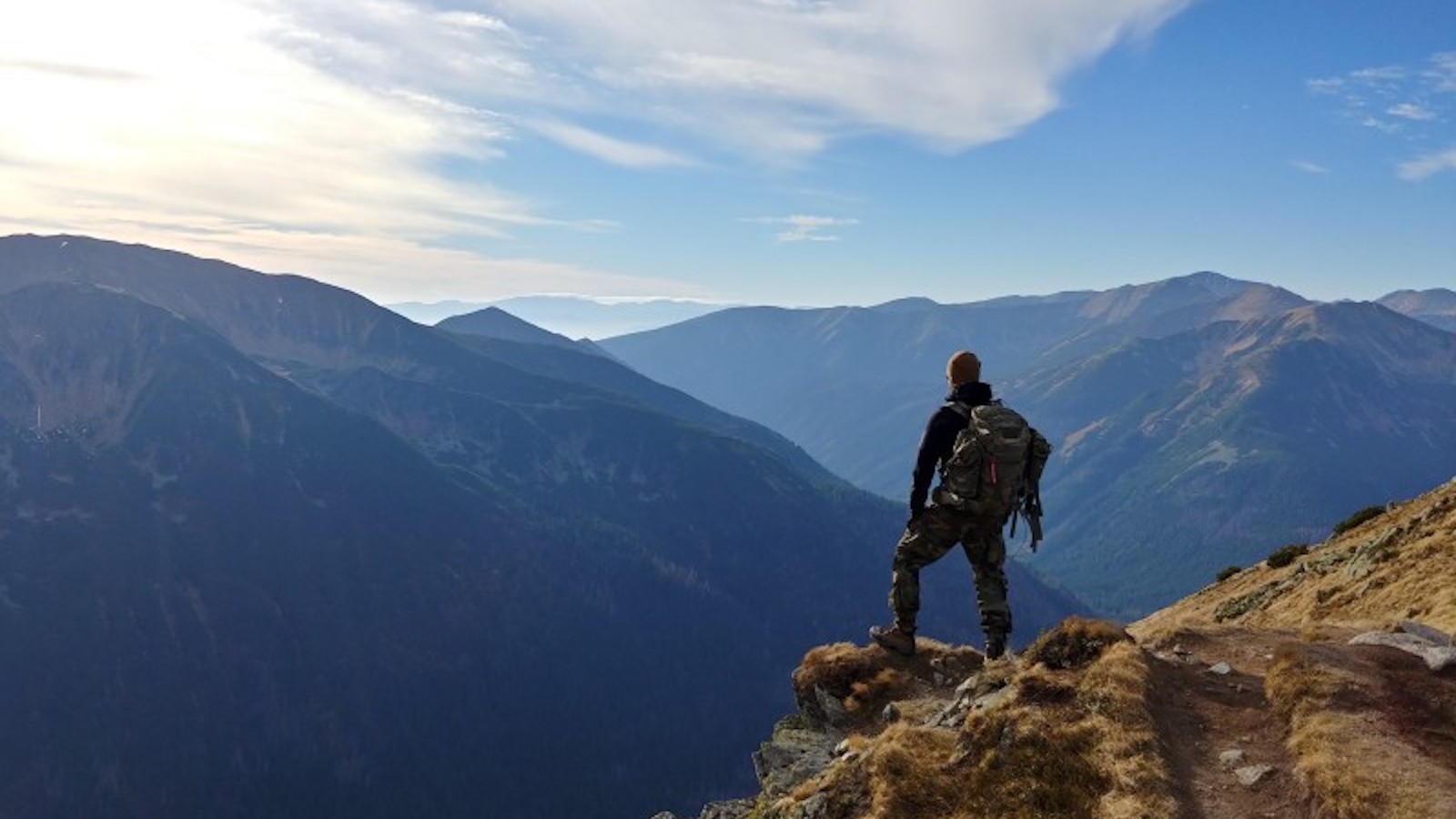 Person with backpack standing on a mountain facing away