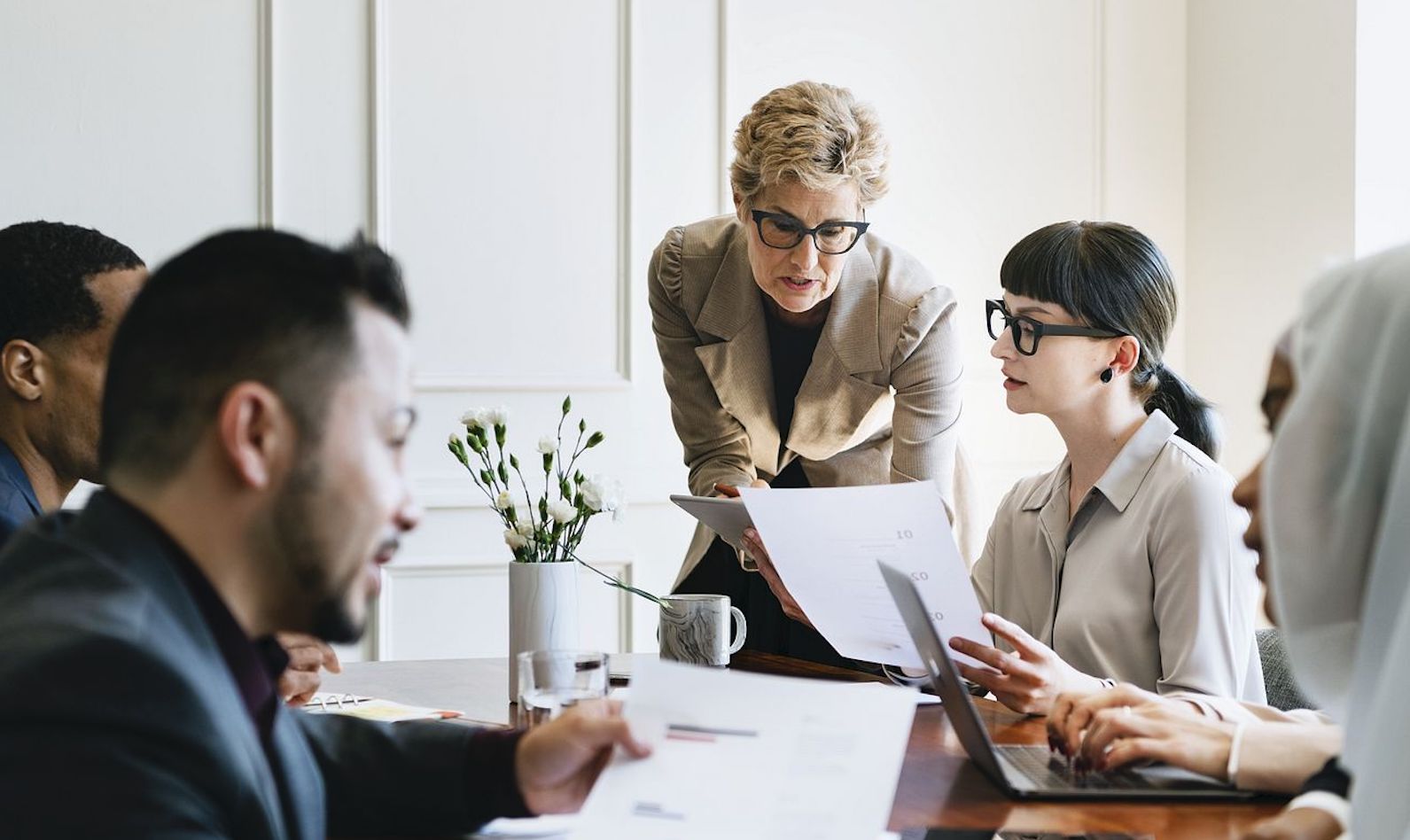 Five people in business in an office and around a desk and looking over papers