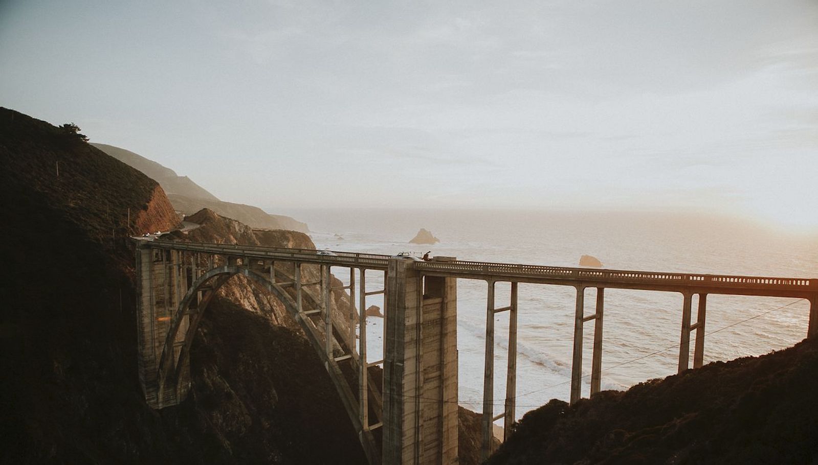 A long bridge in front of a large body of water on a foggy day