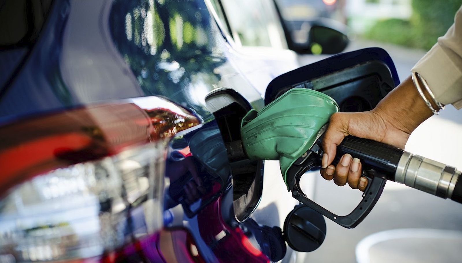 Close-up image from behind of a hand holding a green gas pump up to a blue car