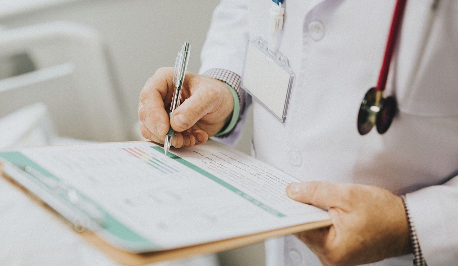 Doctor in a white coat holding a clipboard with a stethoscope and writing something