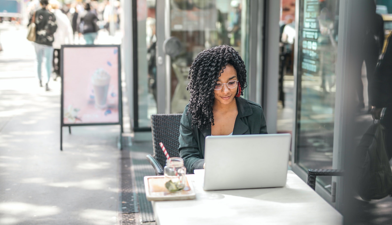 A woman sitting at a table outside a glass building working on a laptop