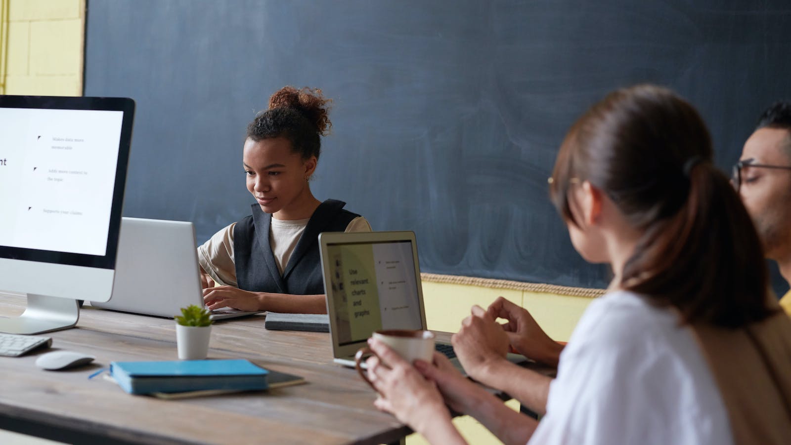 People on a laptops in a classroom with a blackboard