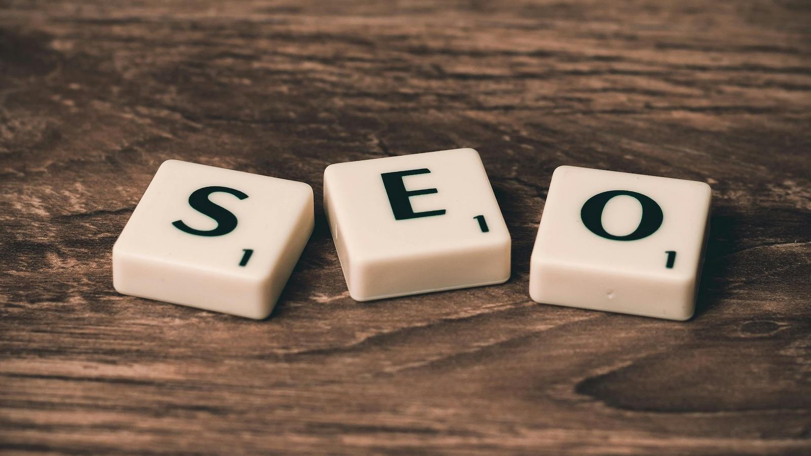 Three White-and-black Scrabble Tiles that spell out "SEO" on Brown Wooden Surface