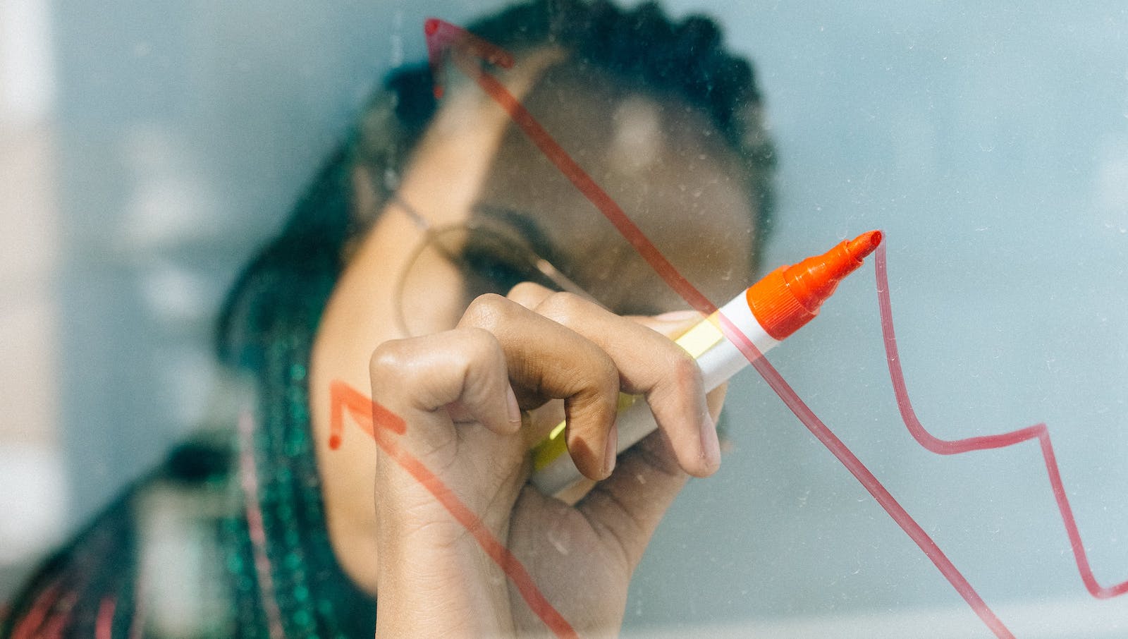 Woman in a Beige Coat Writing on a Glass Panel Using a Whiteboard Marker