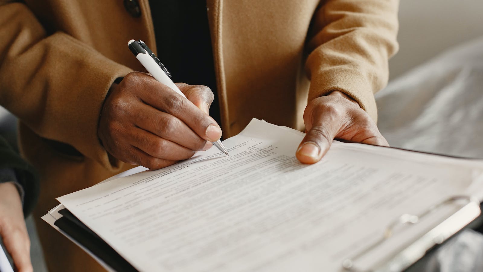 A Person Writing on White Paper while Holding a Pen