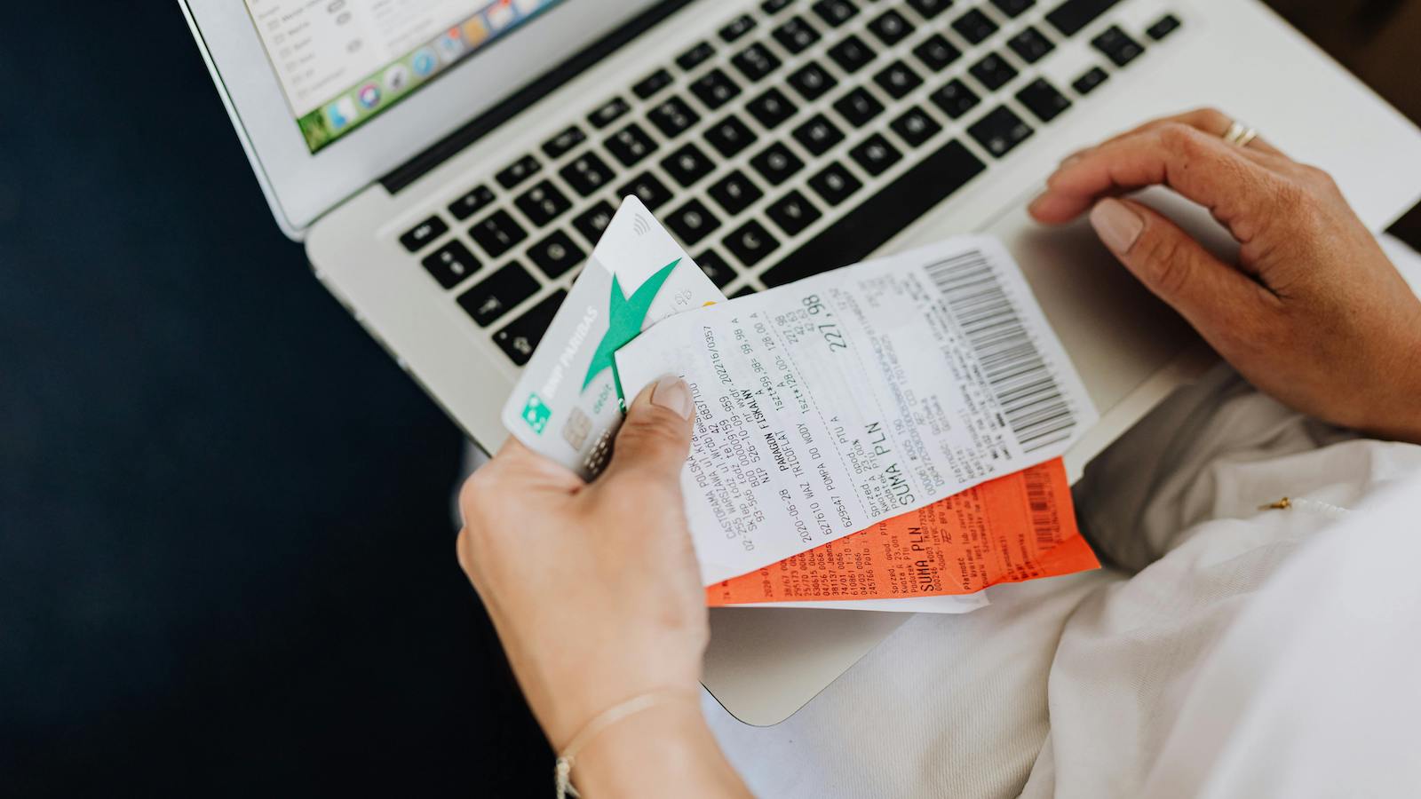 Person Using a Computer and Holding a Credit Card and Receipts