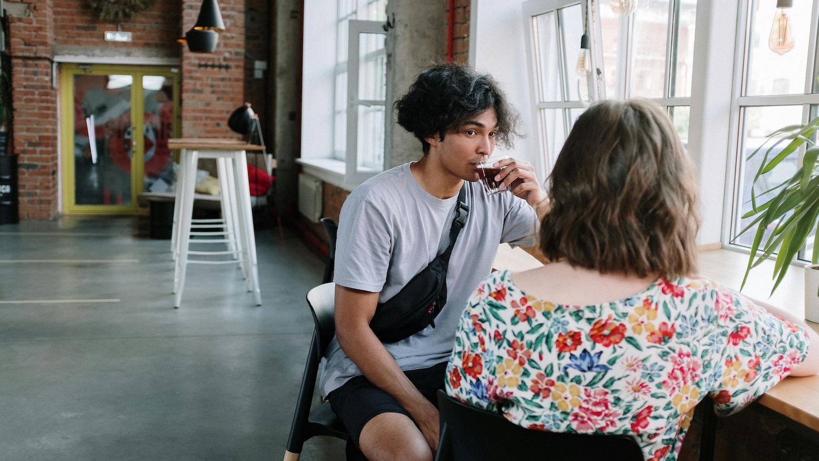 Two young people sitting in a cafe with windows drinking espresso