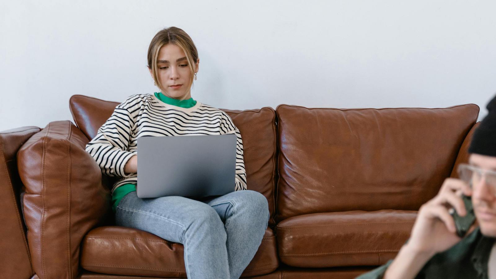 A Woman in a Black and White Stripe Shirt and Blue Denim Jeans Sitting on Brown Sofa