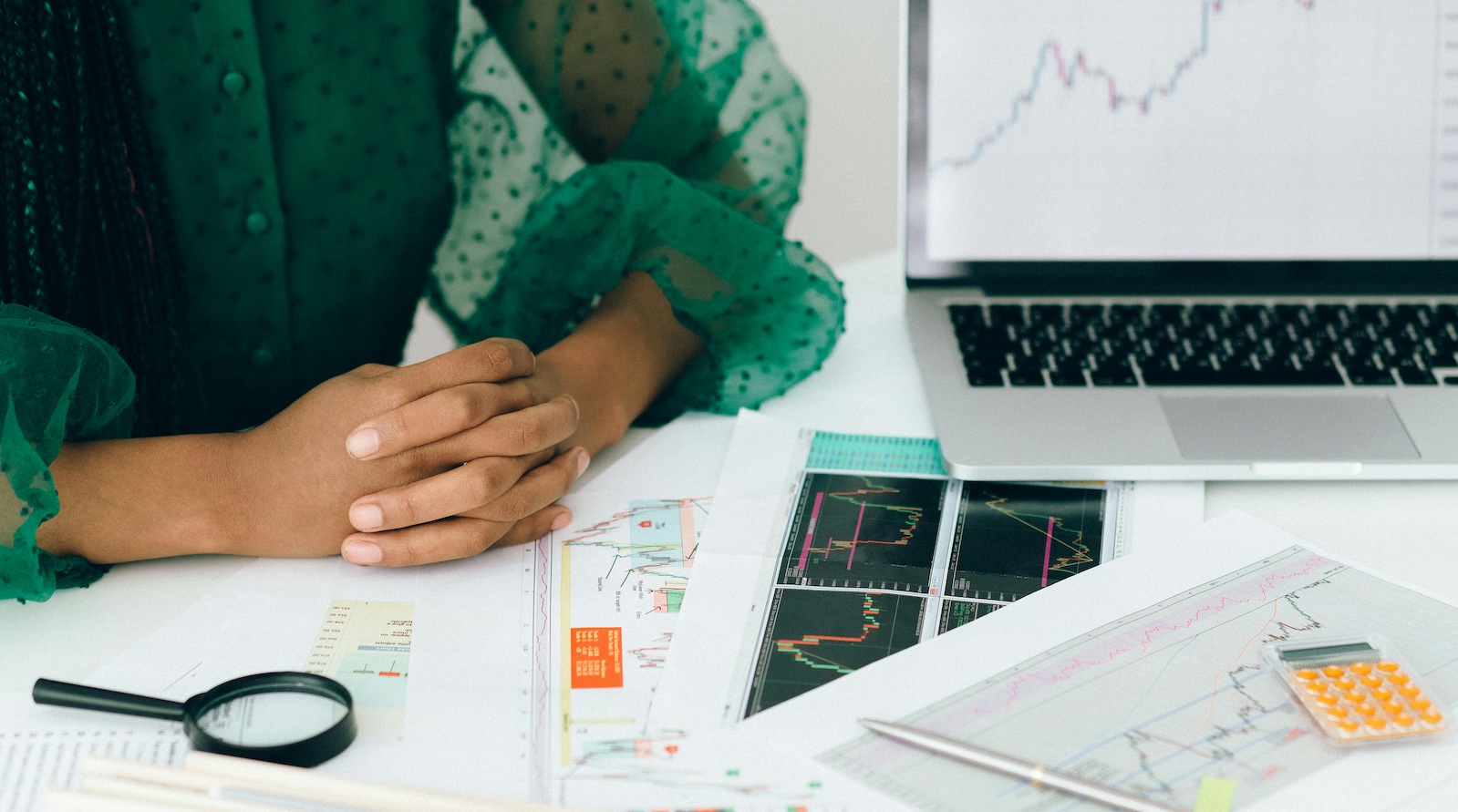 A person sitting at a desk in a green top with a lop and papers on the desk showing charts and graphs