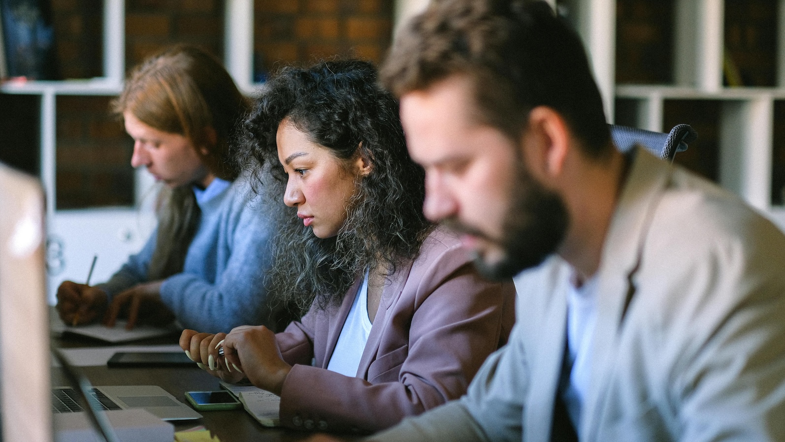Three people in a row sitting at computers looking concerned