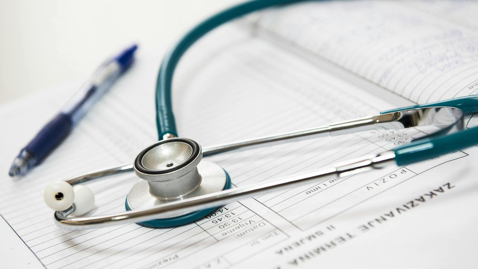 A stethoscope and pen resting on a medical report in a healthcare setting.