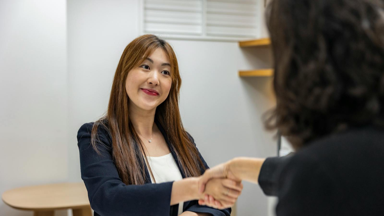 Businesswoman in professional attire shaking hands with recruiter in an office setting.