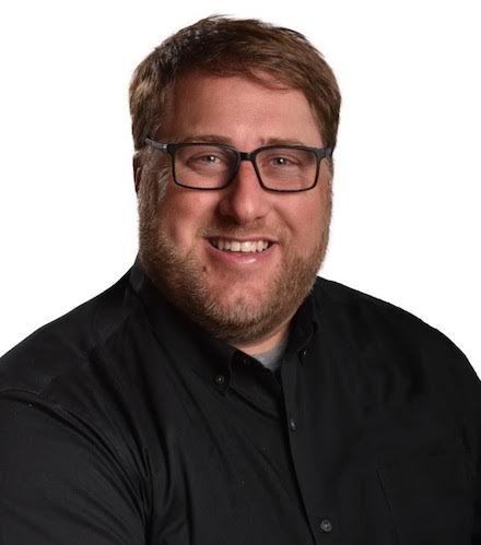 a headshot of Joel Zwicker wearing a black button down shirt 