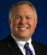 a headshot of Mark Walls wearing a black suit and tie