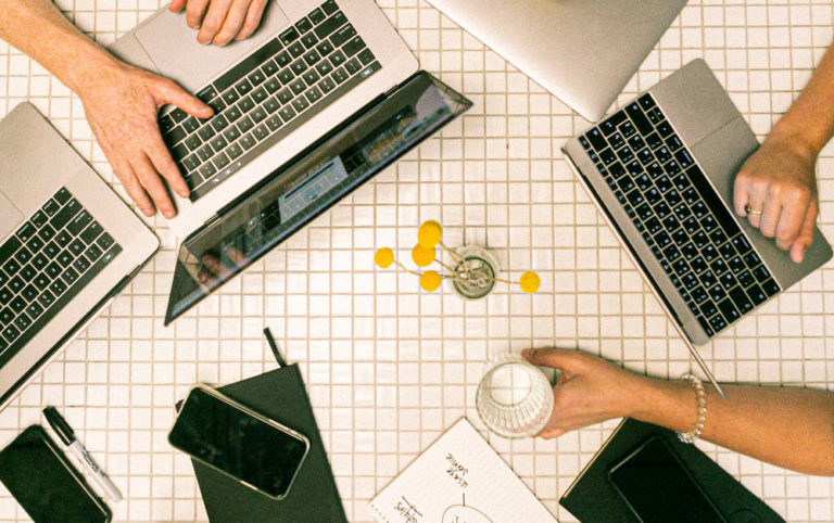 a photo of a desk with multiple people's hands, laptops, and phones