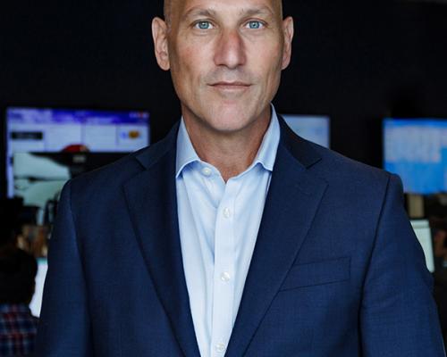 a headshot of Andrew Robinson in a navy blue suit standing in front of computers