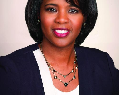A headshot of Marie Carr. She is wearing a black suit and white shirt sitting in front of a eggshell white background. 
