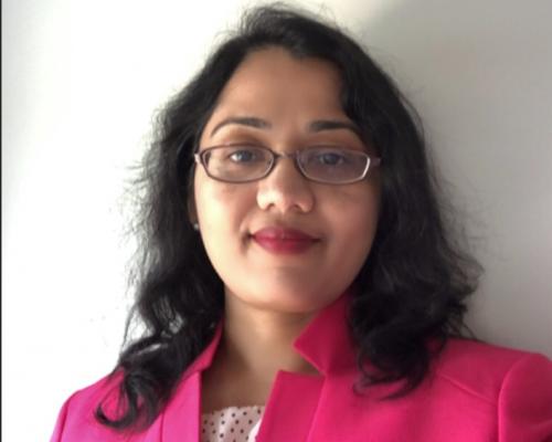 a photo of Preetha Sekharan she is standing against a white background and wearing a bright pink jacket