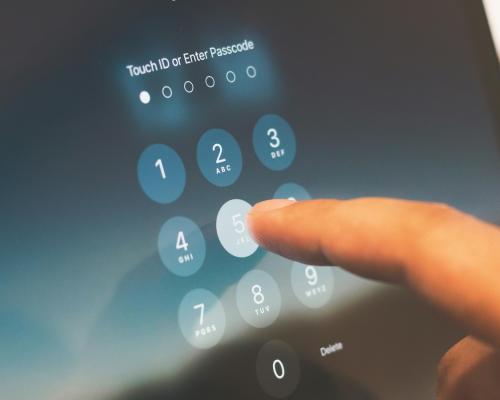 Index finger on a screen typing in a six digit passcode starting with 5