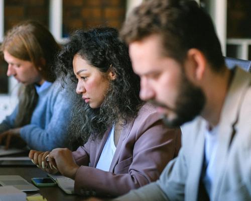 Three people in a row sitting at computers looking concerned