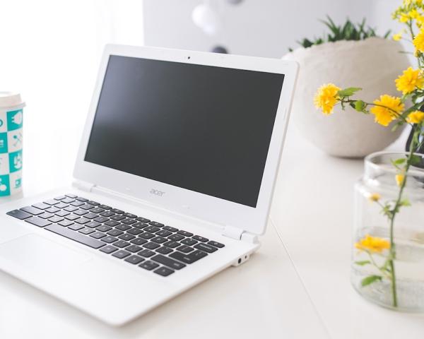 Laptop on a white counter with yellow flowers in a glass next to it and a blue glass