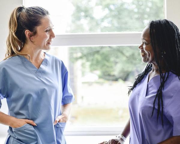Two women in blue and purple scrubs talking to each other in a hospital