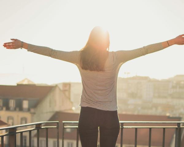 Woman in White Long Sleeve Shirt Standing Near White and Gray House during Daytime