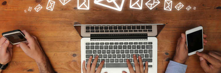 a photo of three sets of hands on a wooden table. Two people are holding smartphones and one is typing on a silver laptop. There are drawings of email symbols above all three sets of hands. 