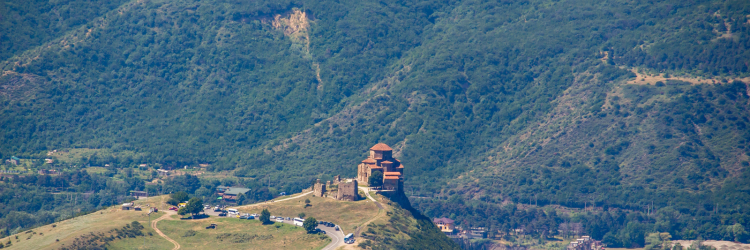 a photo of a castle on a hill nestled in between mountains covered in green trees