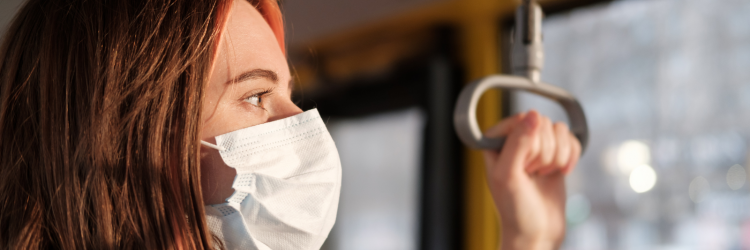 a photo of a brunette women standing on the bus wearing a white surgical mask 