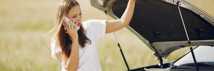 Woman calling on the phone next to the open hood of a car