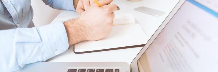 Person holding pen and notebook sitting by a computer