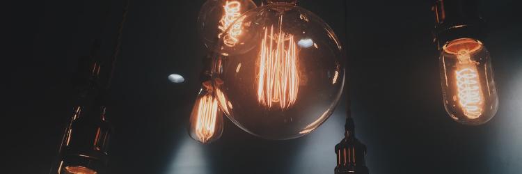 Six light bulbs of various sizes hanging from a ceiling and lit up