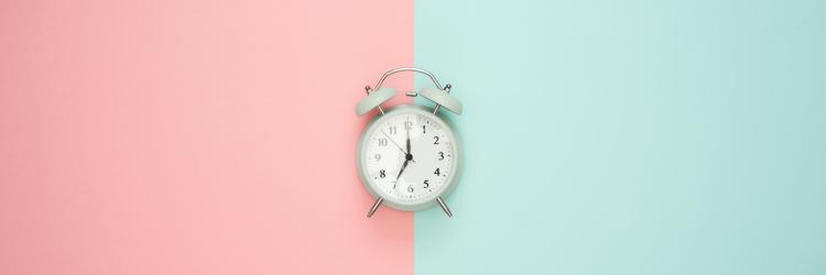 An analog clock set to seven o'clock against a half pink and half blue background