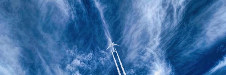 Below view of a plane with a trail against a blue sky with wispy clouds