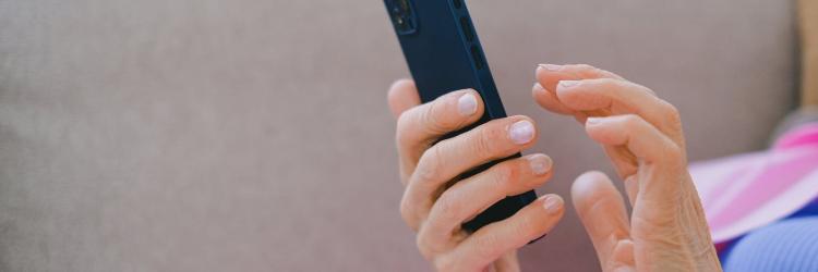 A close-up image of a person's hands holding a black phone