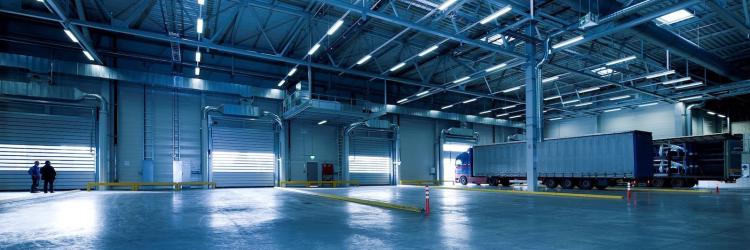 The inside of a mostly empty warehouse with one large truck, all under blue lighting