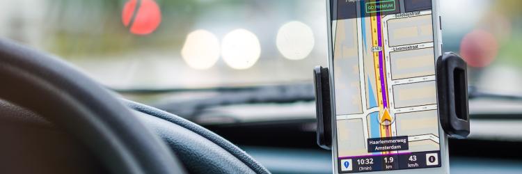 Close-up image of a smartphone with a map on the screen and on the dashboard of a car
