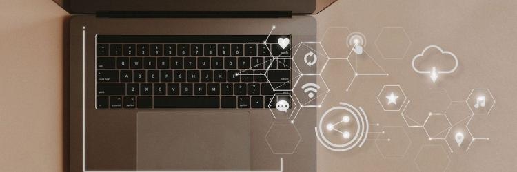 Overhead view of a laptop with white and translucent digital icons coming out of keys on the computer
