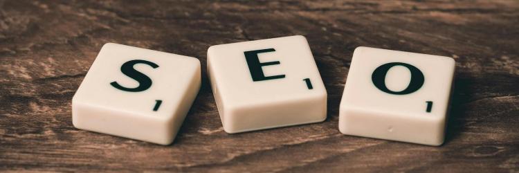 Three White-and-black Scrabble Tiles that spell out "SEO" on Brown Wooden Surface